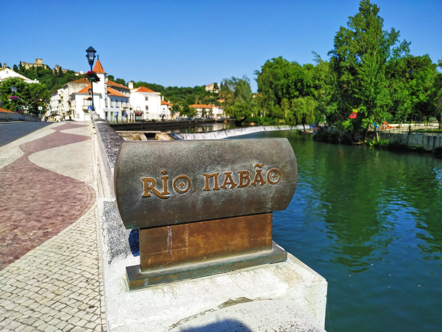 Placa en el río Nabão, destacando el nombre del río con el Castillo de Tomar al fondo.